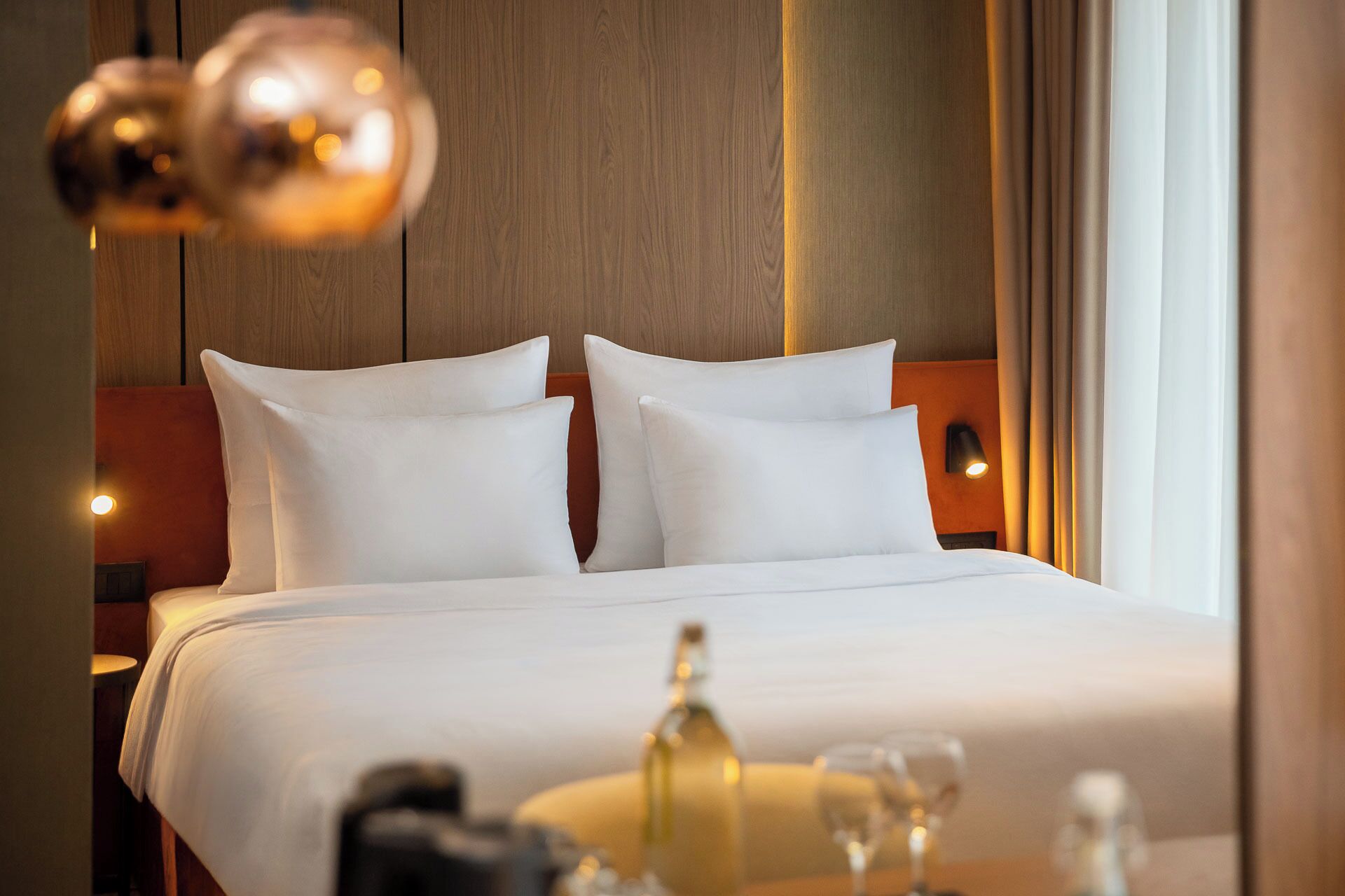 Une chambre d’hôtel avec un lit, des oreillers, une table de chevet, une bouteille et des verres.