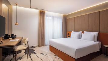 A hotel room with a bed, a desk, a chair, and a small table.