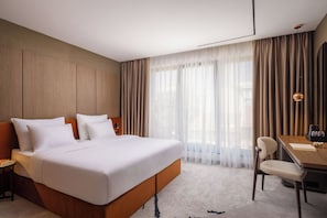 A modern hotel room with a large bed, a desk, and a chair.
