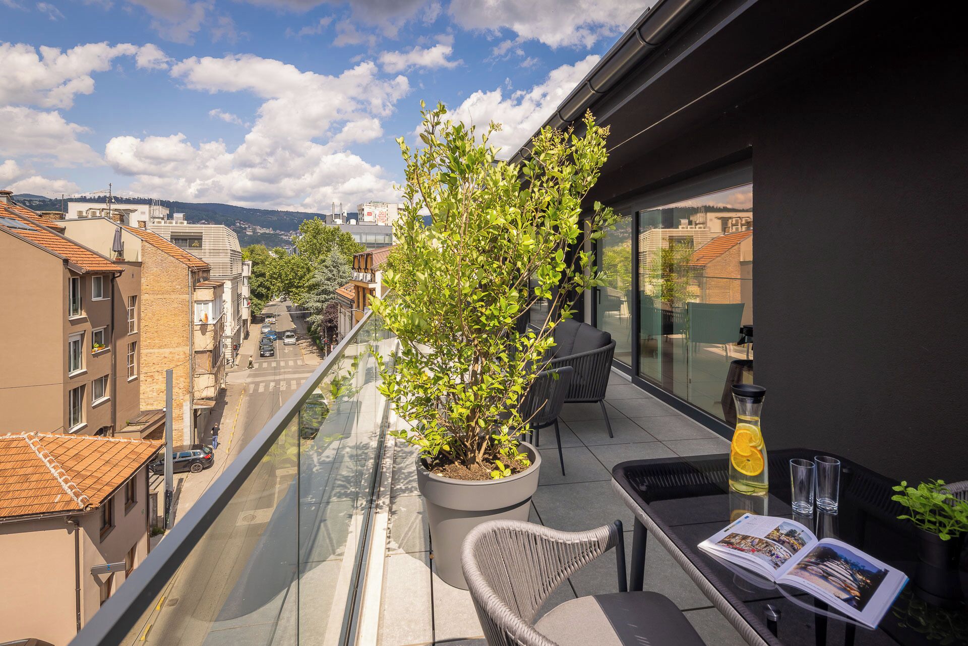 Een balkon met een bloempot, een glazen tafel met een tijdschrift en een drankje.