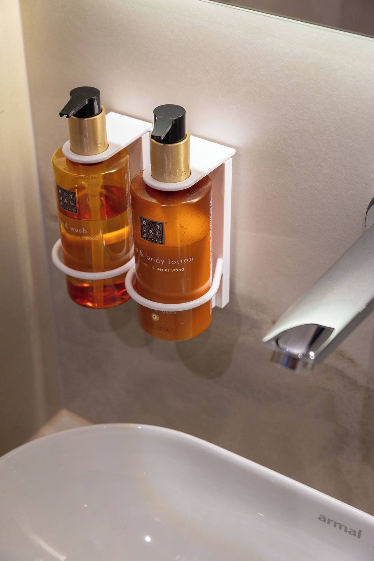 Baño con un lavamanos blanco y dos botellas de loción corporal sujetas a un dispensador de pared.