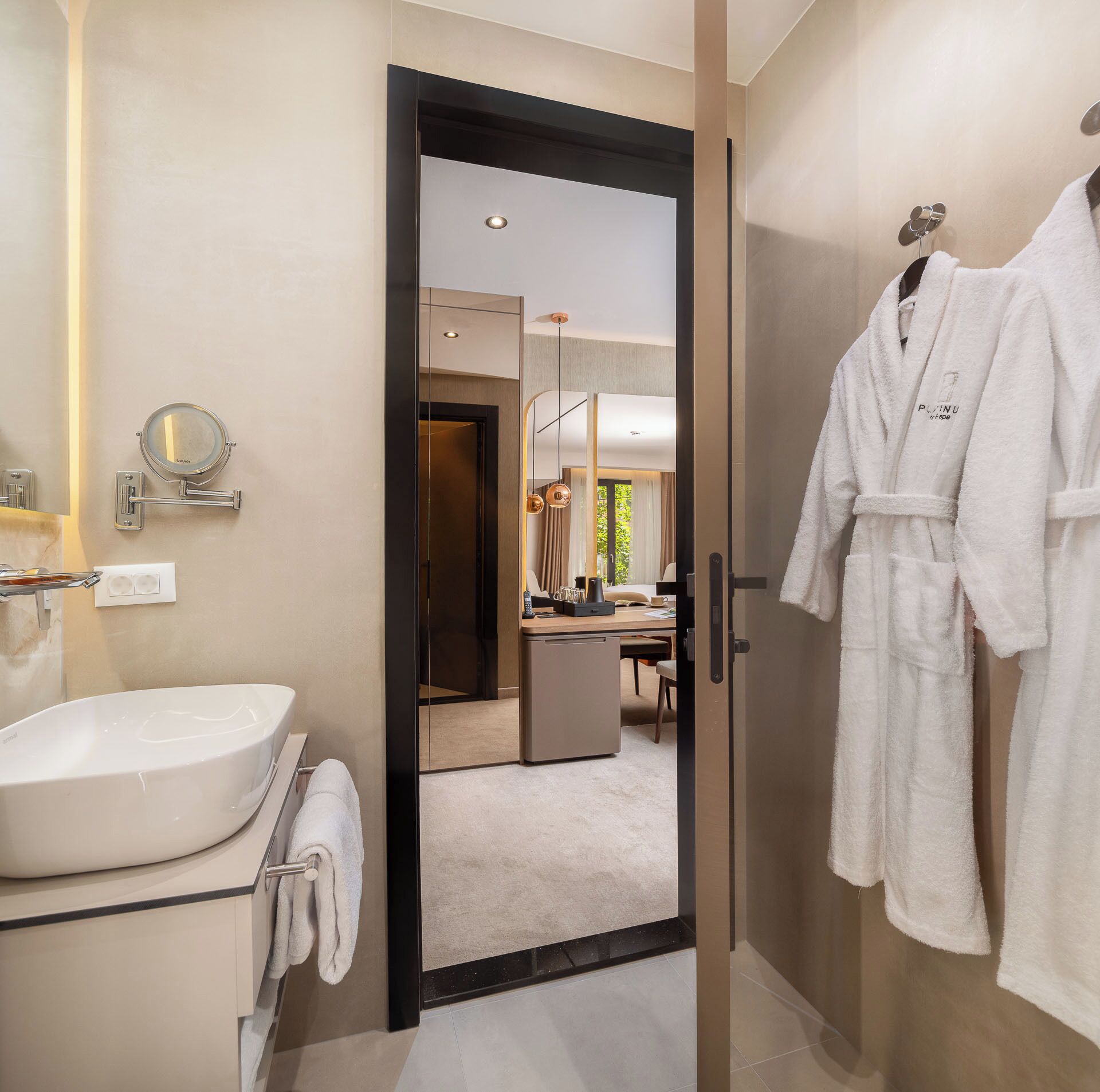 A modern bathroom with a large mirror, a sink, and a robe hanging on a hook.
