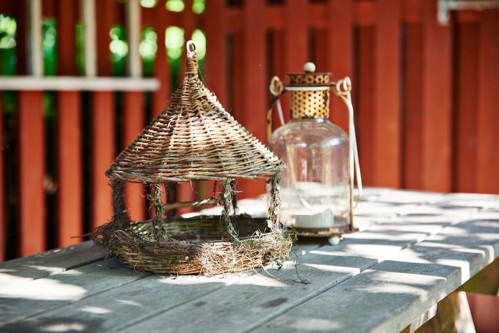 A wicker birdhouse with a glass lantern beside it on a wooden table.