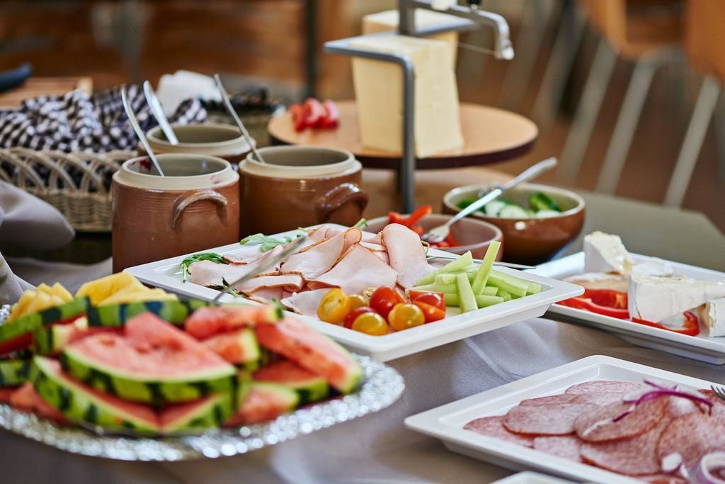 Una mesa con diversos alimentos, como fiambres, verduras y queso, además de tazas y un bol de ensalada.