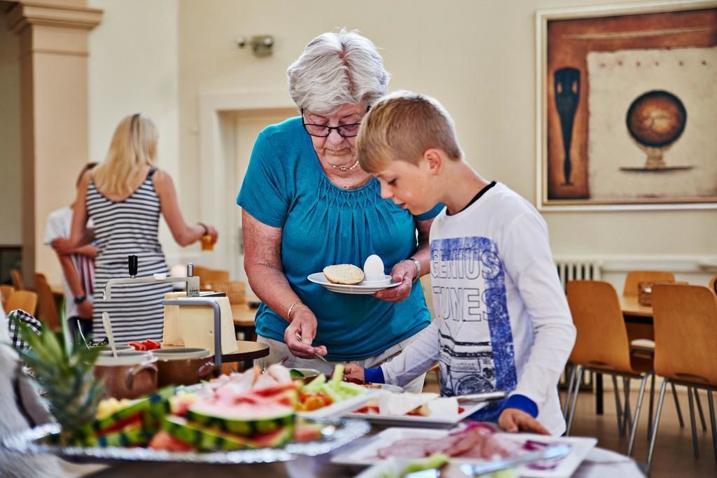 Un comedor con una barra de buffet, con diferentes alimentos y una persona sirviendo comida a otra.