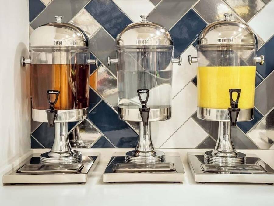 Three beverage dispensers with transparent containers and metallic bases, set against a tiled backsplash.
