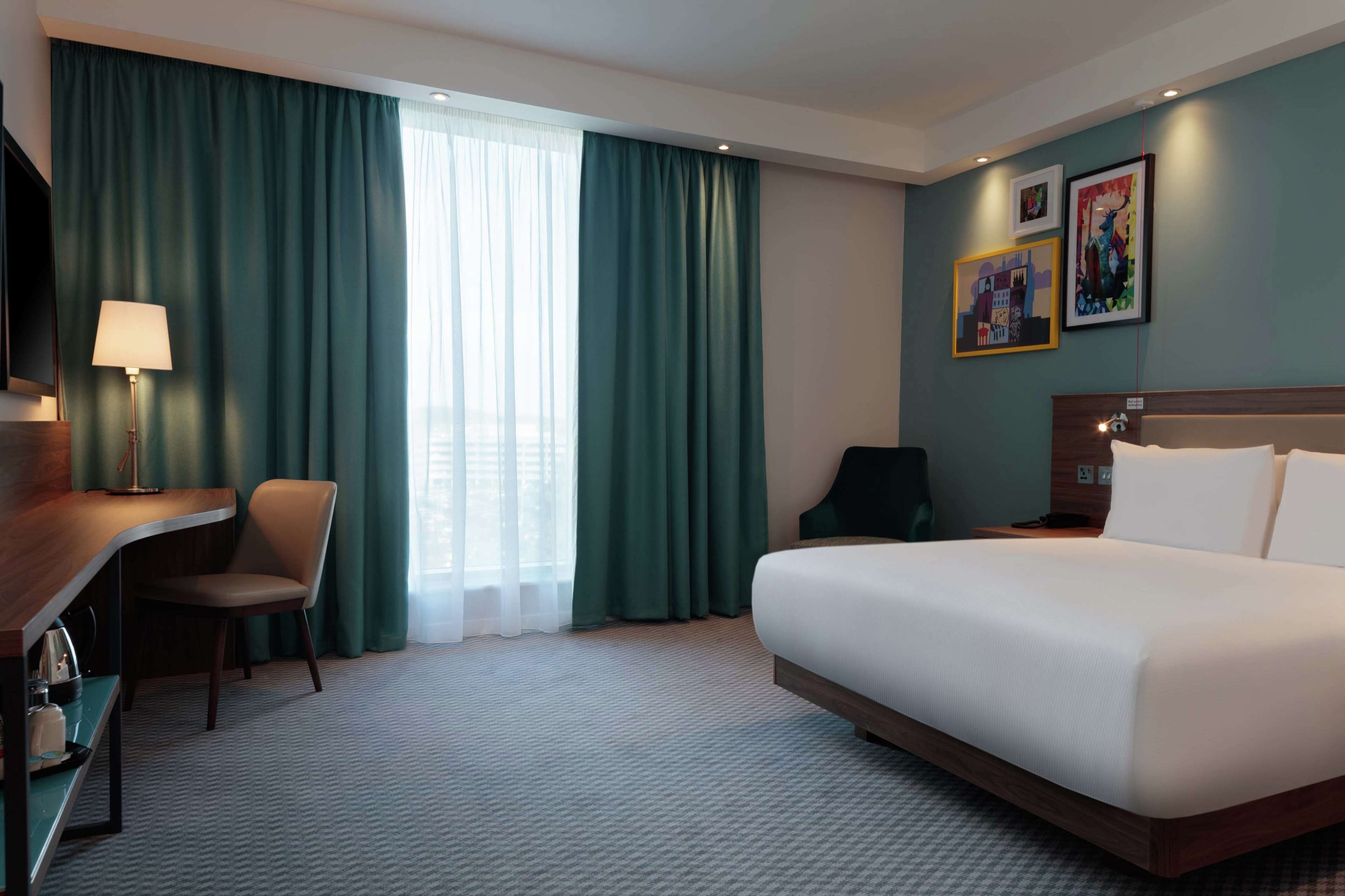 A hotel room with a bed, a desk, a chair, and a TV.