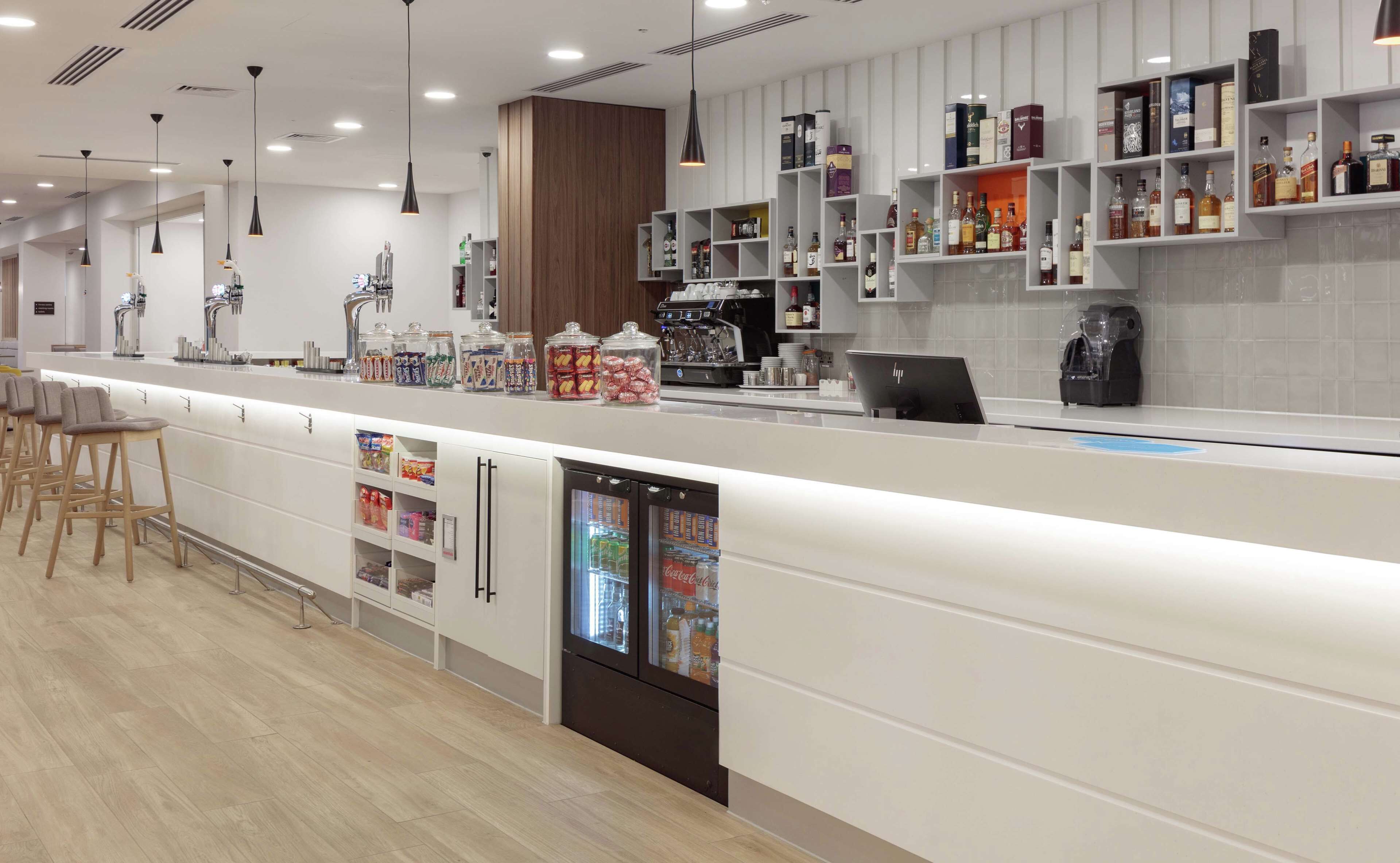 Un espace bar moderne doté d’un long comptoir, de sièges et d’un présentoir réfrigéré.