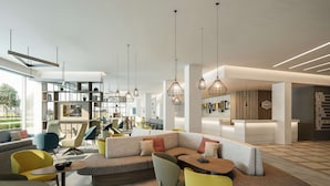 Un hall d’hôtel moderne avec un canapé modulable, des fauteuils colorés et des luminaires suspendus.