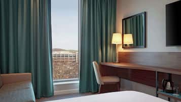 Habitación de hotel con cama, escritorio, silla, lámpara, televisor y vista a un estacionamiento.