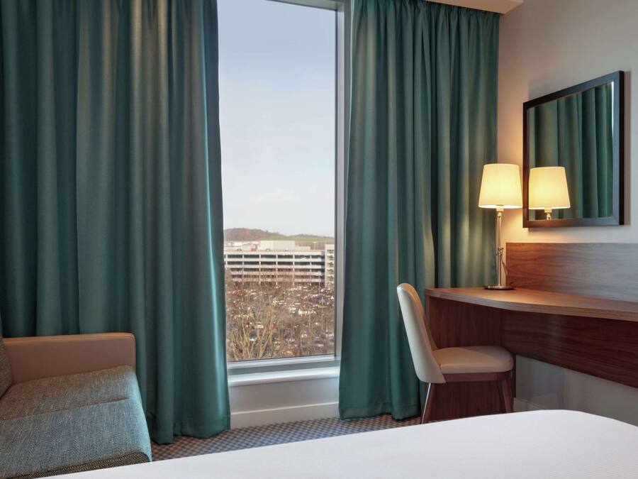 Habitación de hotel con cama, escritorio, silla, lámpara, televisor y vista a un estacionamiento.