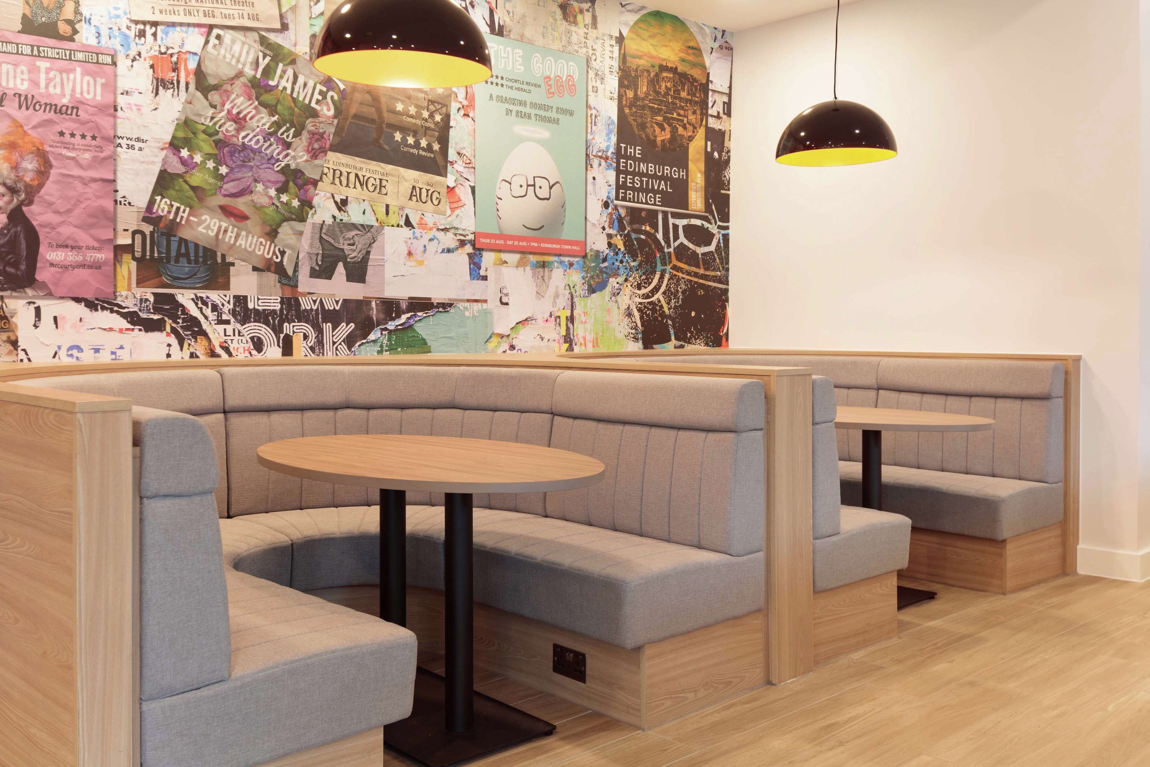 A modern interior with curved seating and round tables, featuring a wall adorned with various posters and a black pendant light.