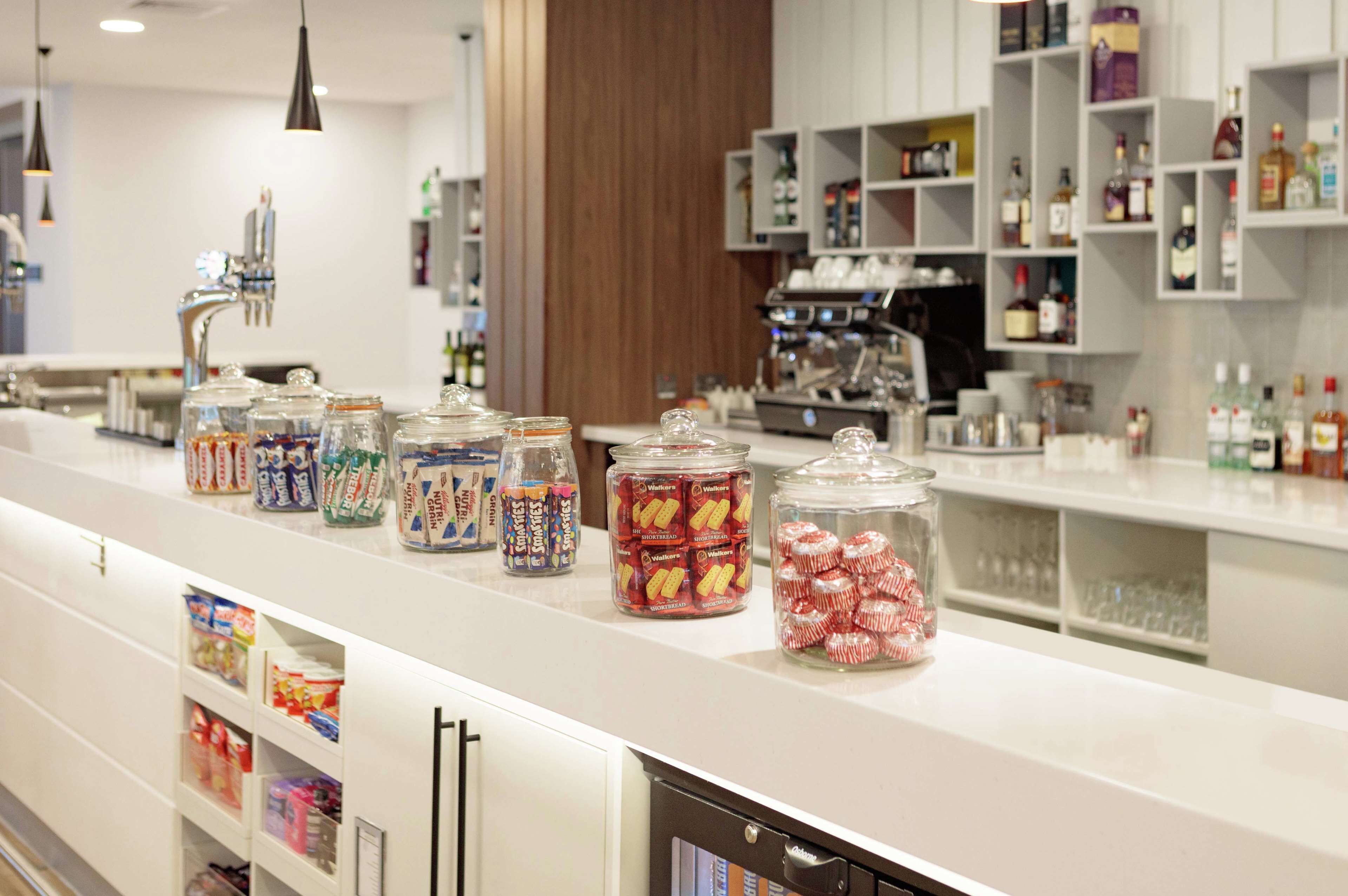 A bar area with a white counter, various jars of snacks, and shelves with bottles.