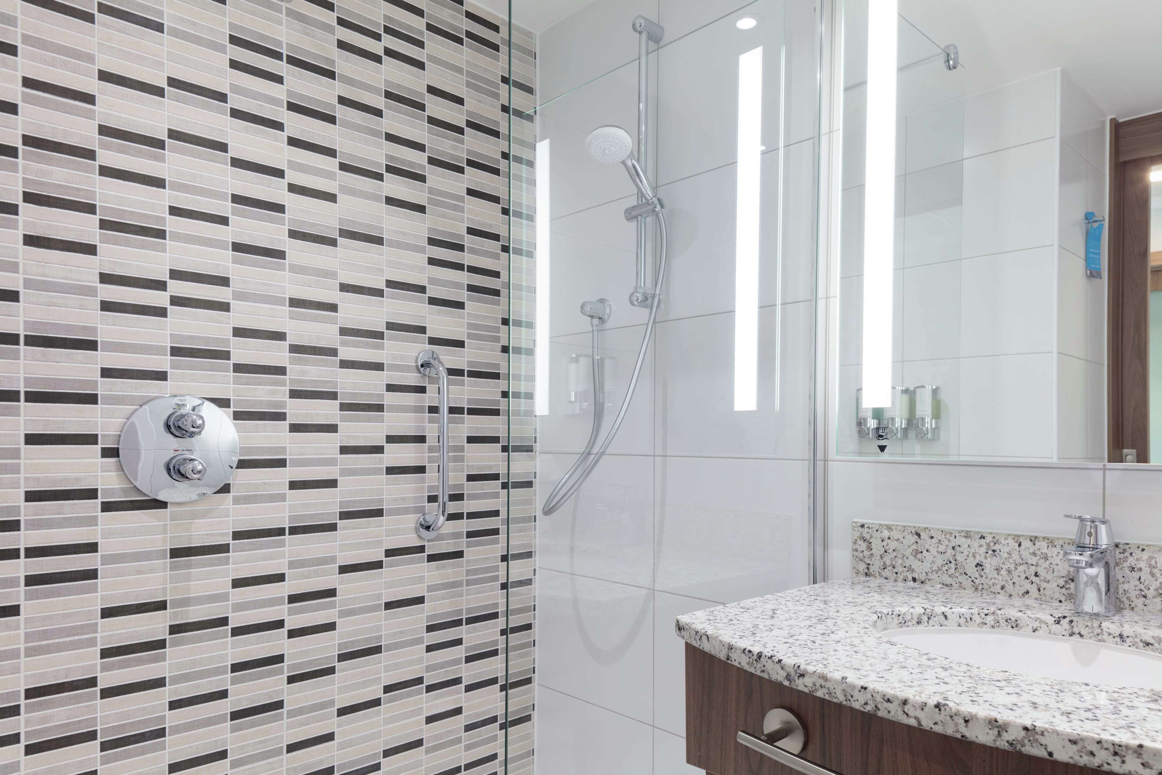 A modern bathroom with a patterned tile wall, a glass shower enclosure, and a granite countertop sink.