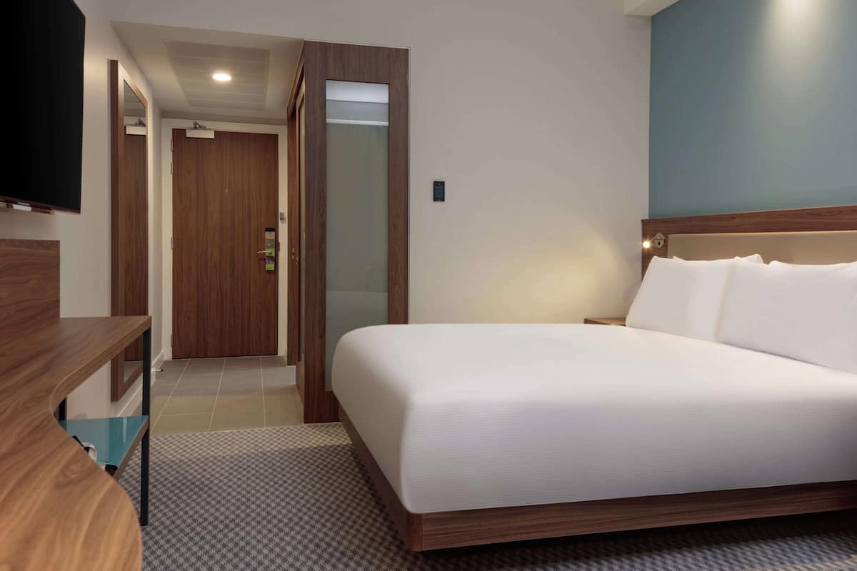 A hotel room with a bed, bedside table, and a television mounted on the wall.