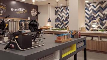 A modern cafe with a central counter, waffle maker, and various food items.