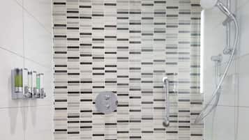 A modern bathroom with a tiled shower area, a handheld showerhead, and a wall-mounted faucet.