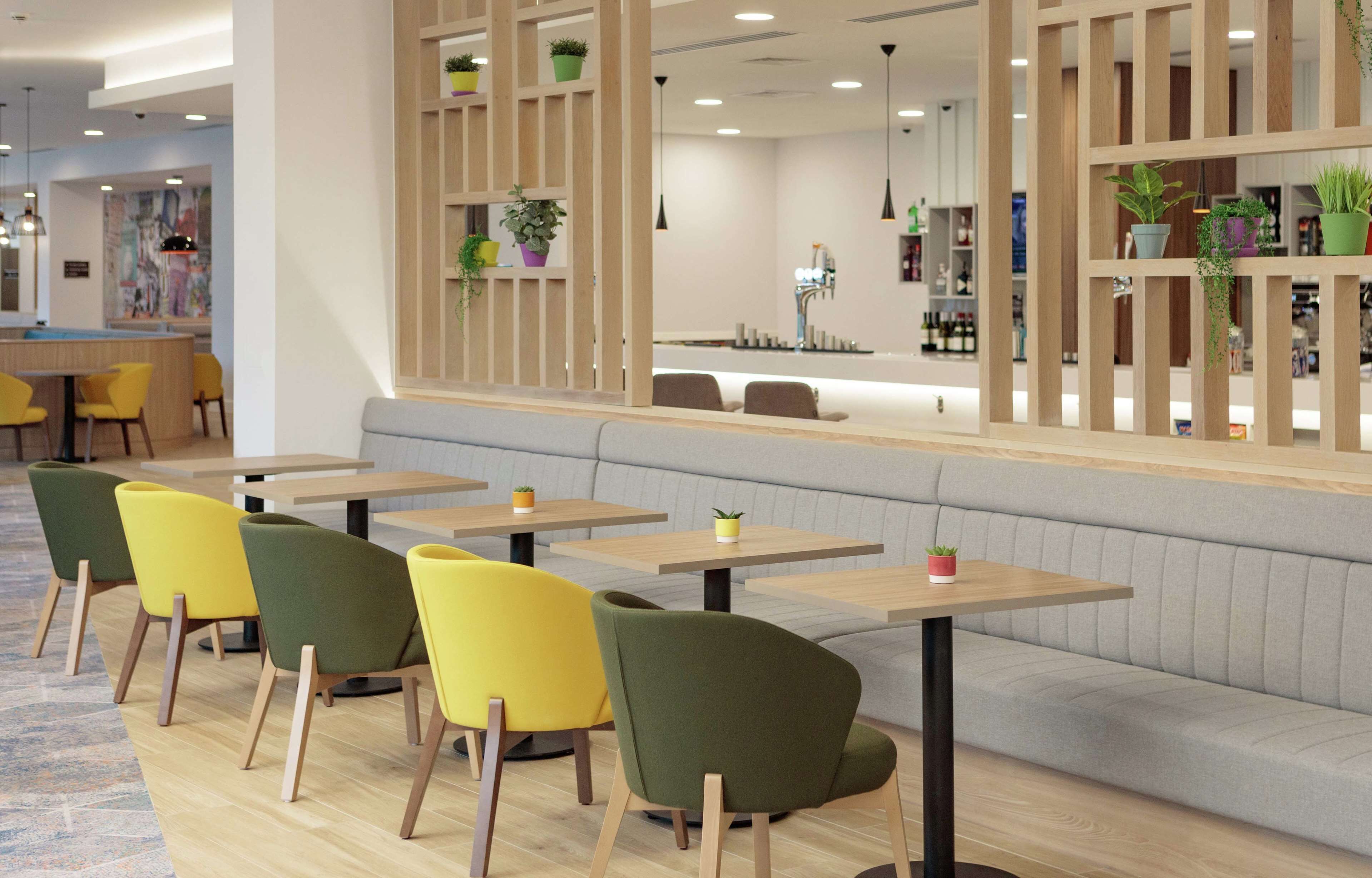 Ein modernes Café mit Holztischen und -stühlen, einer Sitzgelegenheit und Topfpflanzen.