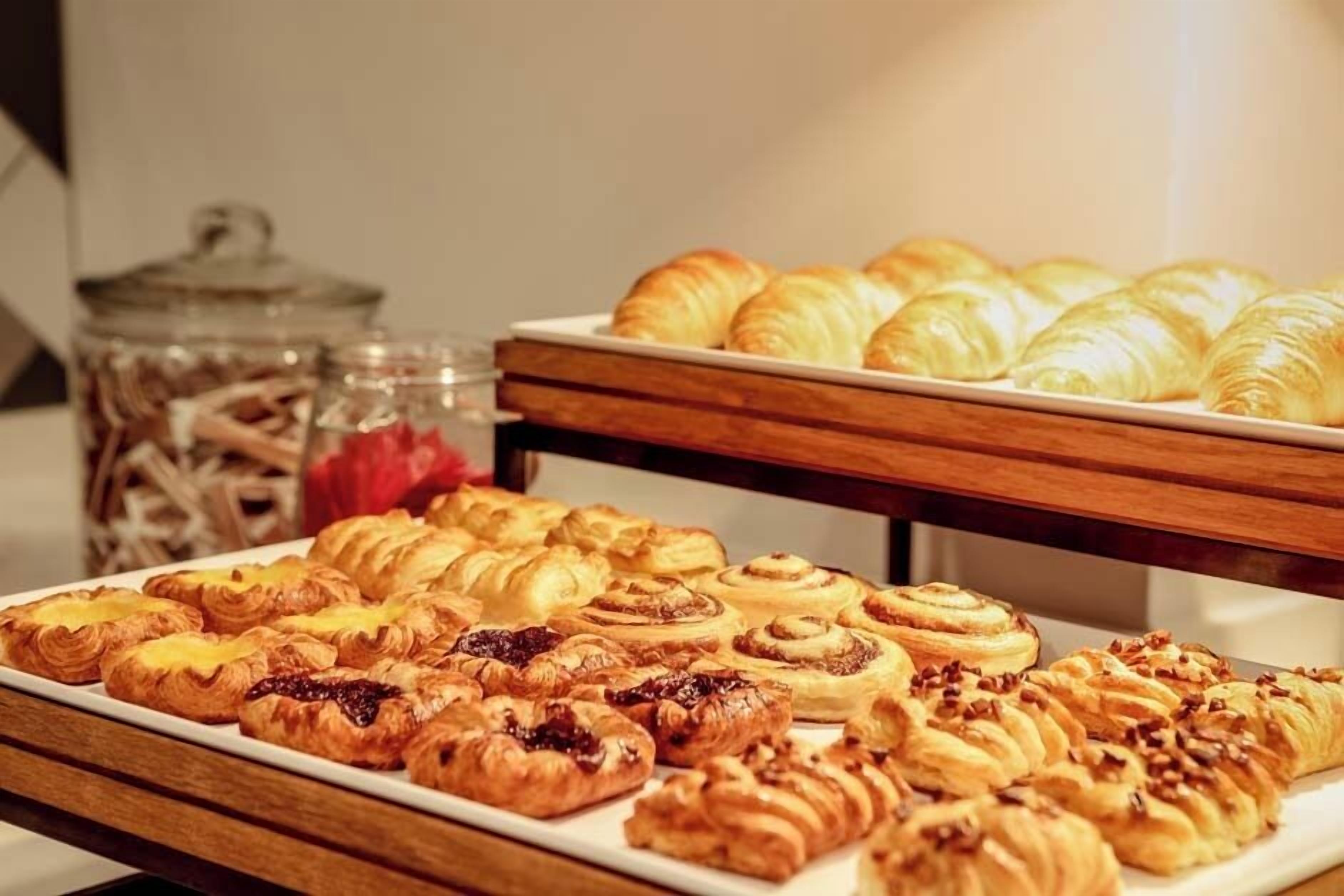 A variety of pastries on display, including croissants and cinnamon rolls, in a buffet setting.