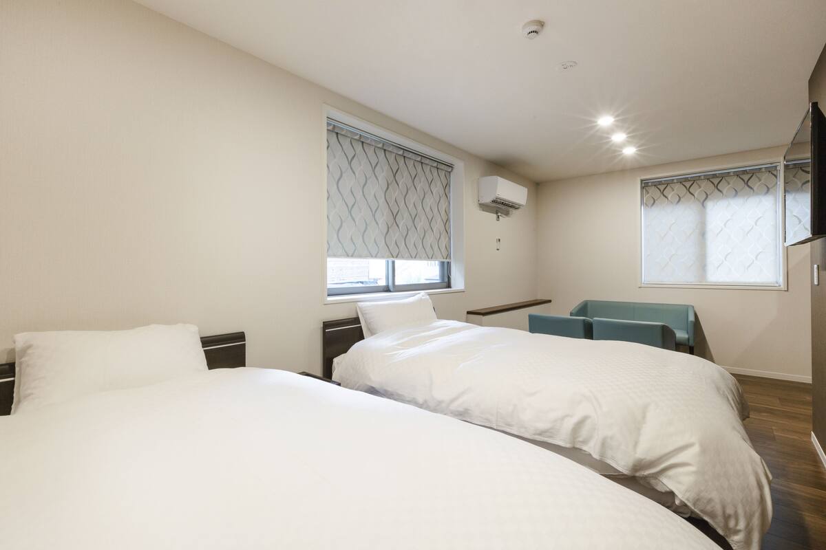 A hotel room with two beds, a desk, a chair, and an air conditioning unit.