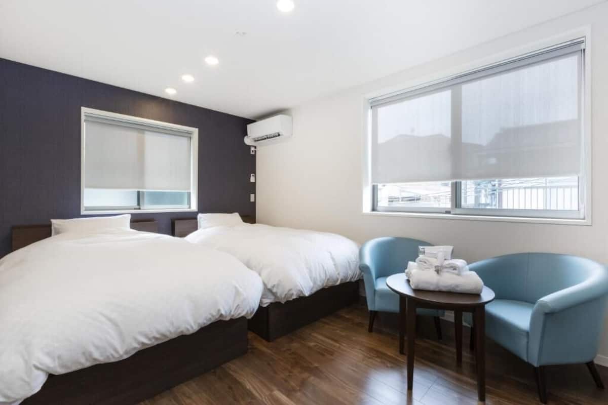 A hotel room with two beds, a small table with towels, a chair, and large windows.