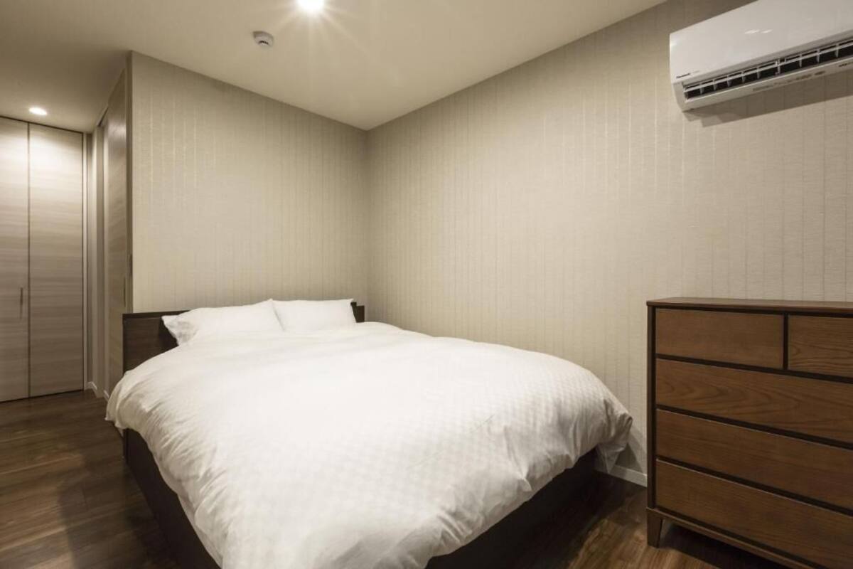 A bedroom with a bed, a dresser, and an air conditioning unit on the wall.
