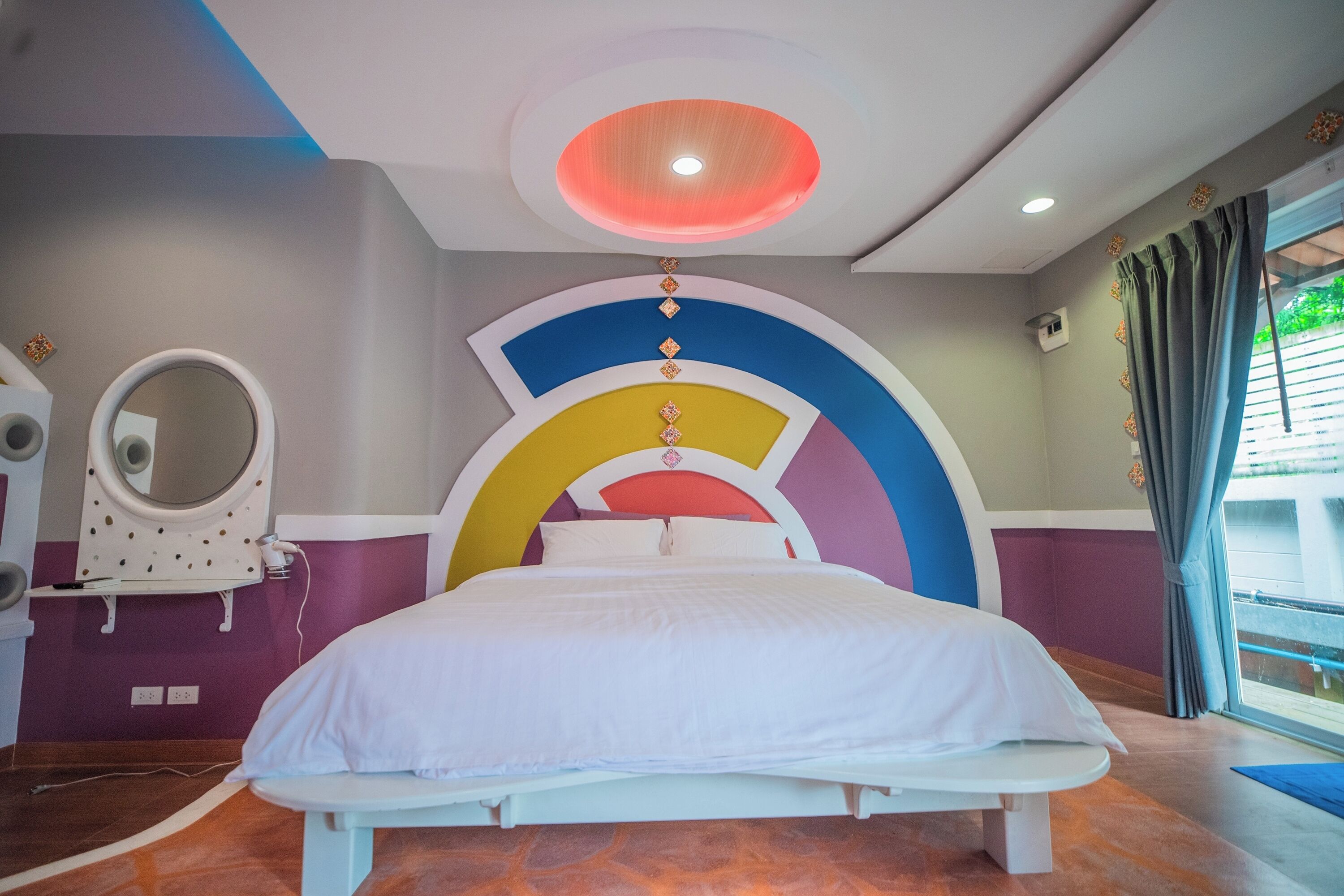 A modern bedroom with a bed, a vanity with a mirror, and a ceiling light fixture.