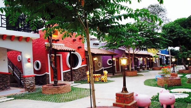 A courtyard with a central fountain, surrounded by buildings with unique architectural designs and a well-maintained garden.