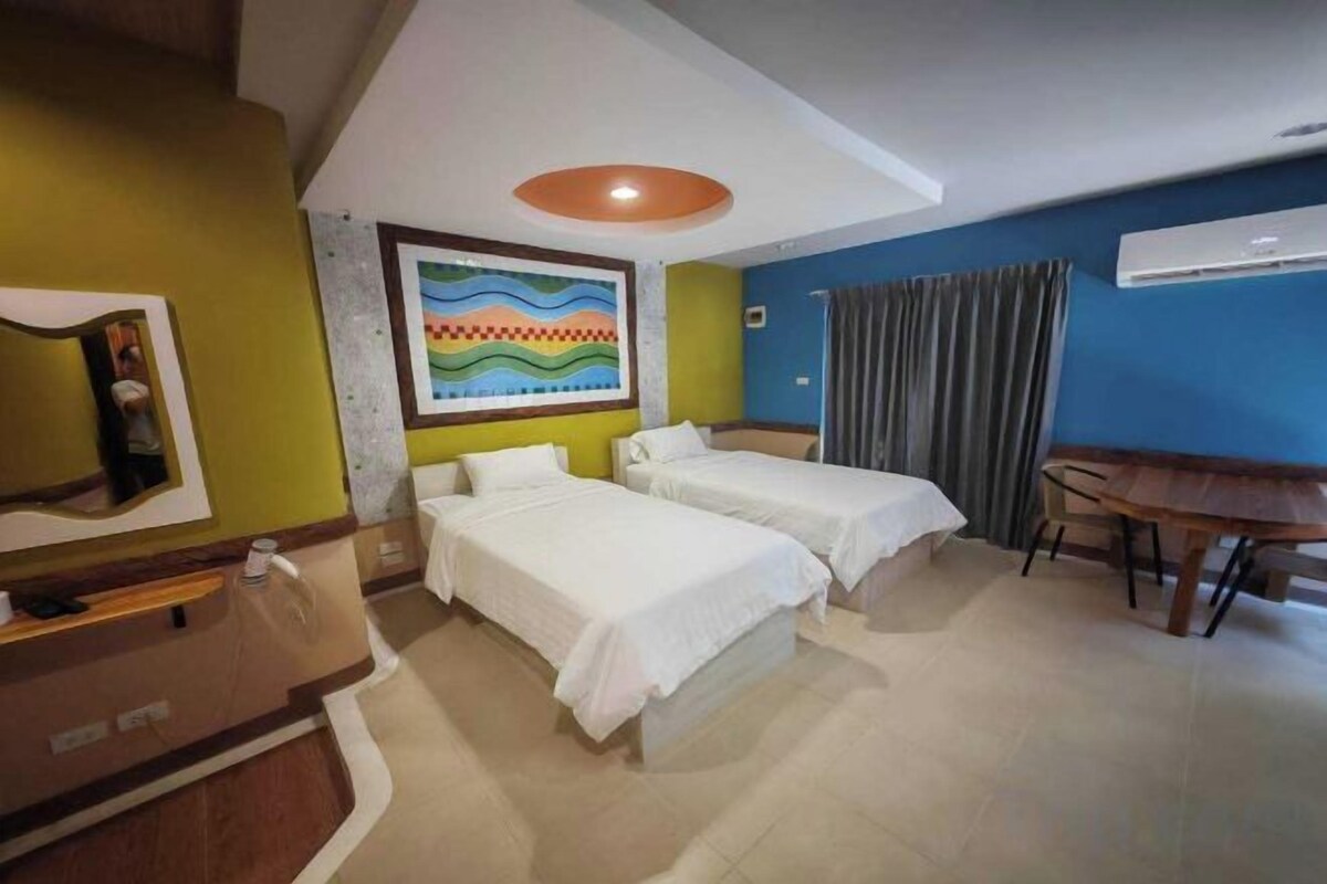 Une chambre d’hôtel avec deux lits, un bureau, une chaise, une télévision et un tableau au mur.