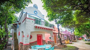 A unique building with a red door, a balcony, and a small outdoor seating area with tables and chairs.