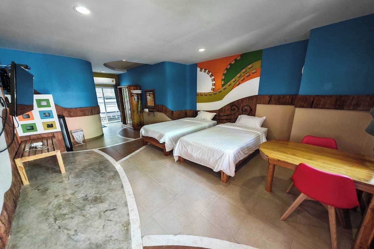 Une chambre d’hôtel avec deux lits, une table en bois et une chaise rouge.