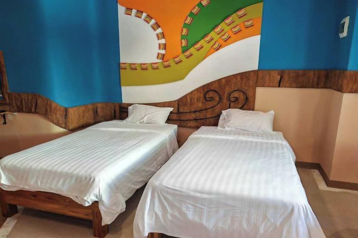 A room with two single beds, a wooden headboard, and a colorful mural on the wall.