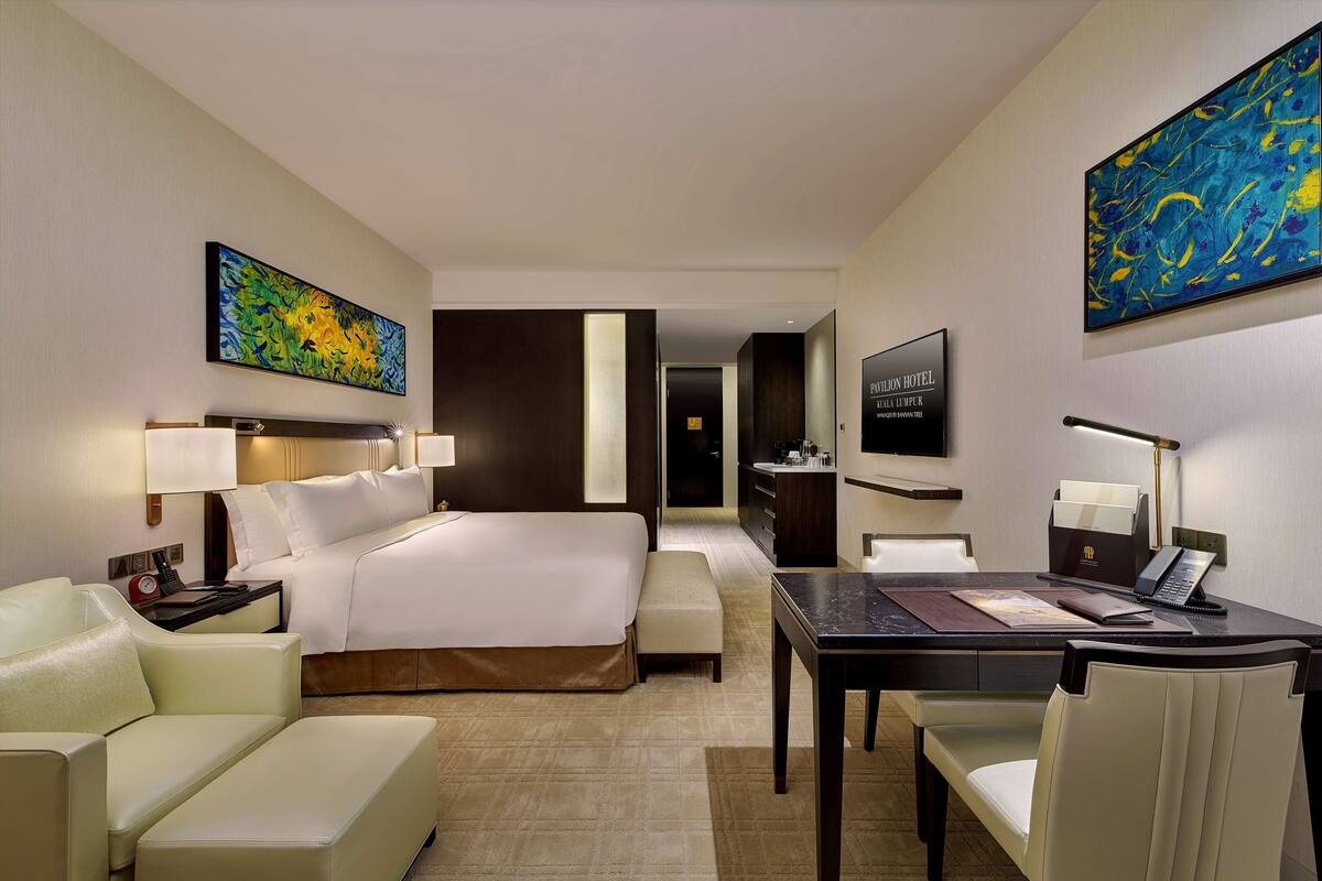 Une chambre d’hôtel comprenant un lit, un bureau, une chaise, un canapé et des œuvres d’art accrochées aux murs.