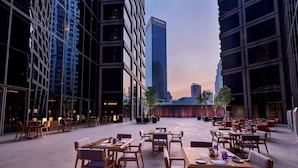 An outdoor dining area with tables and chairs, surrounded by tall buildings. - Pavilion Hotel Kuala Lumpur Managed by Banyan Tree (Kuala Lumpur)
