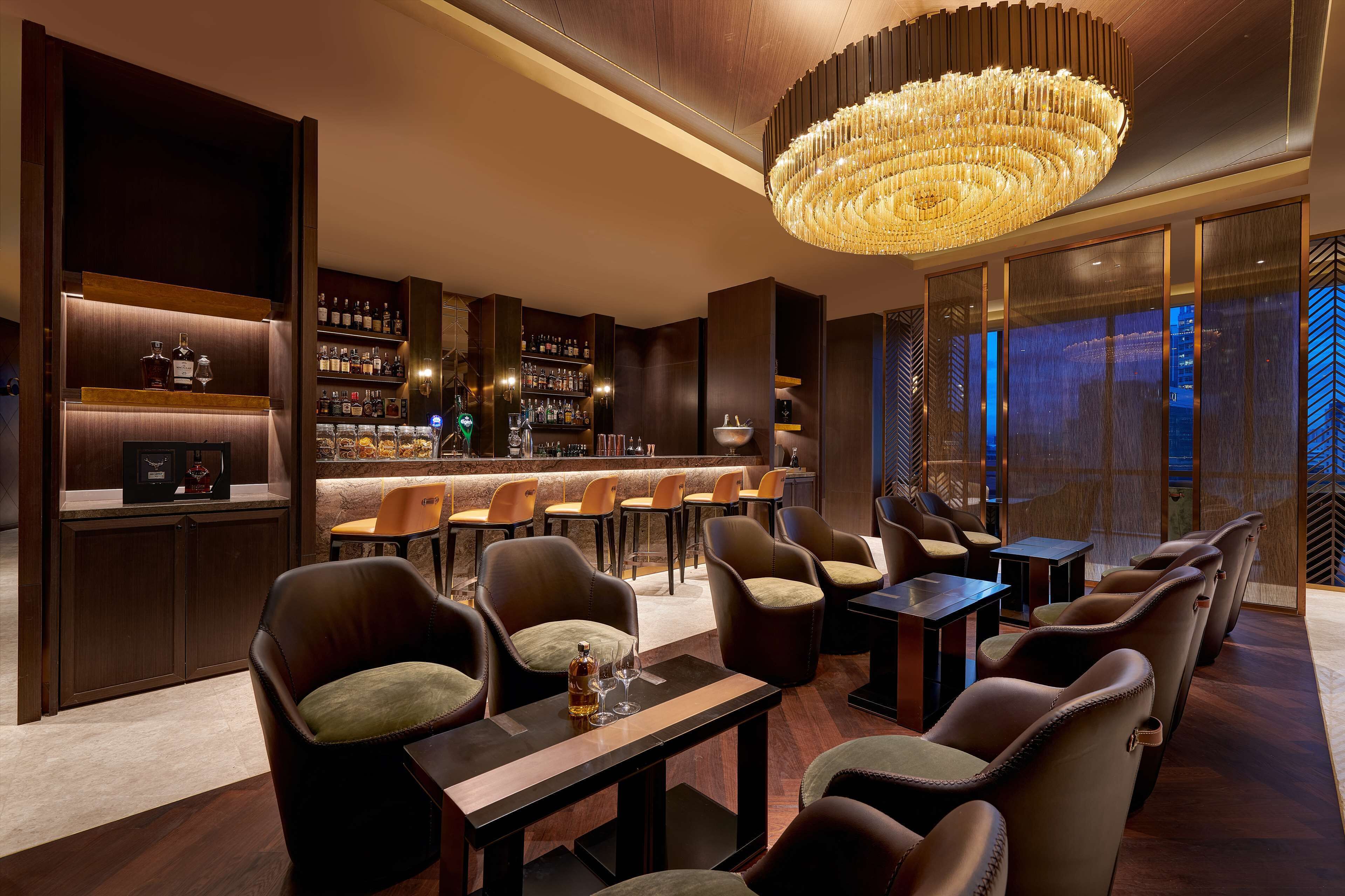 A bar area with leather chairs, a bar counter, and a chandelier.