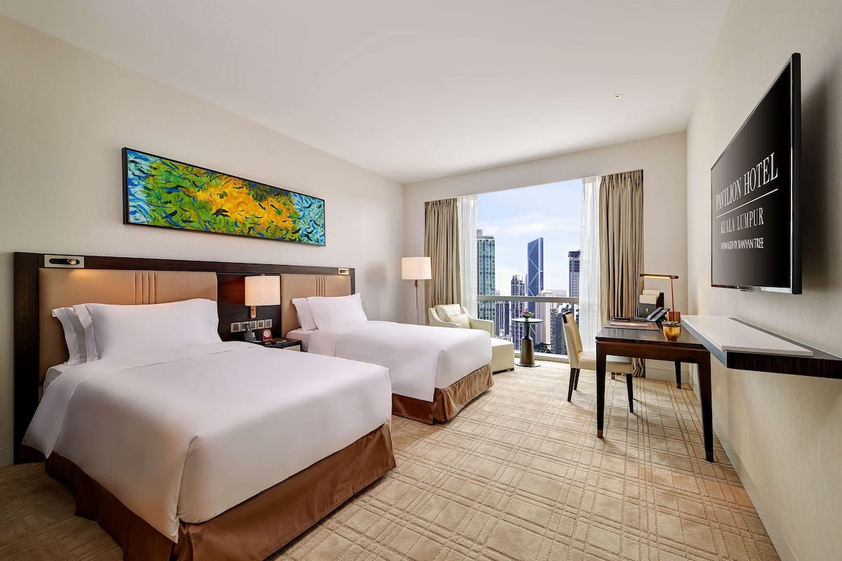Une chambre d’hôtel avec deux lits, un bureau, une chaise, une télévision et une grande fenêtre donnant sur la ville.