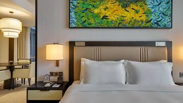 A hotel room with a large bed, a desk with a lamp, a chair, and a painting on the wall.