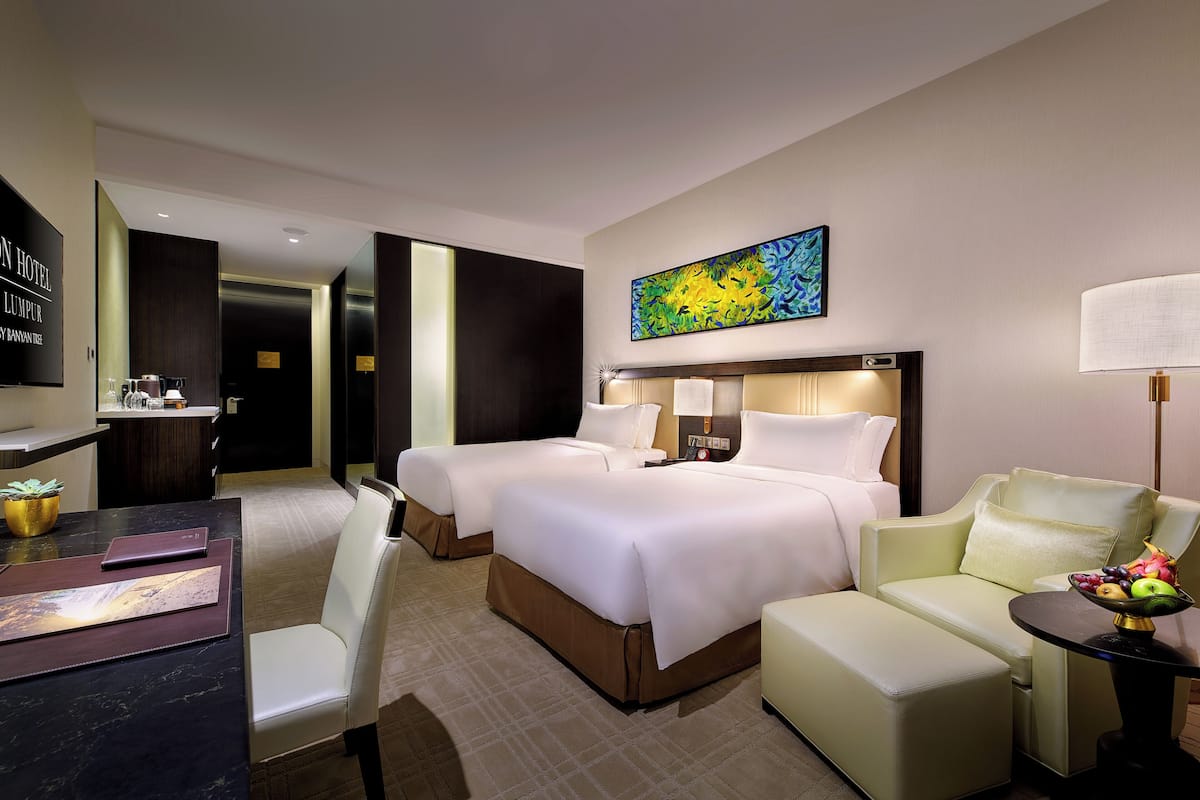 Ein Hotelzimmer mit zwei Betten, einem Schreibtisch, einem Sessel, einer Couch, einer Lampe und einem Bild an der Wand.