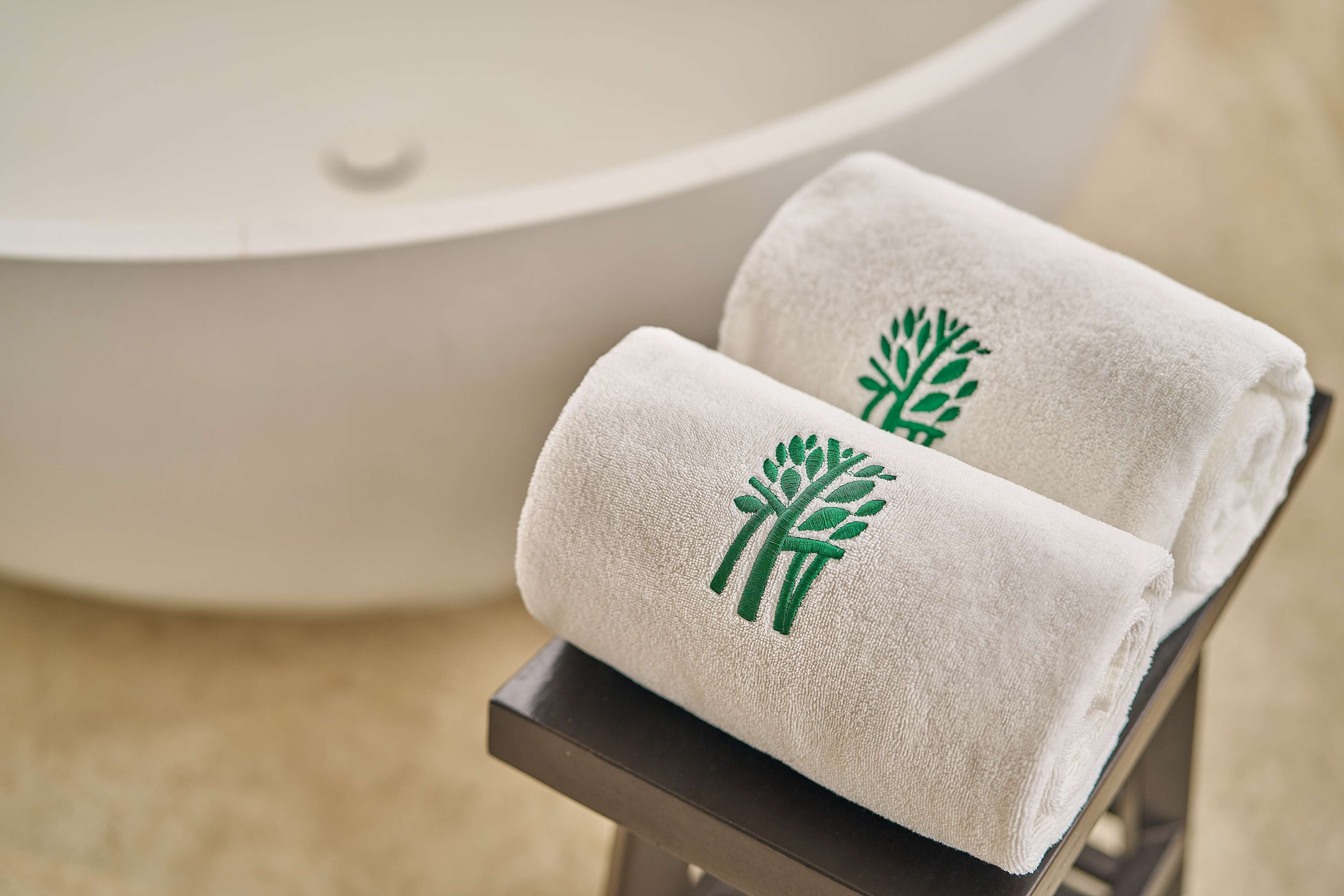 Two white towels with a green tree logo on a black towel rack in a bathroom.