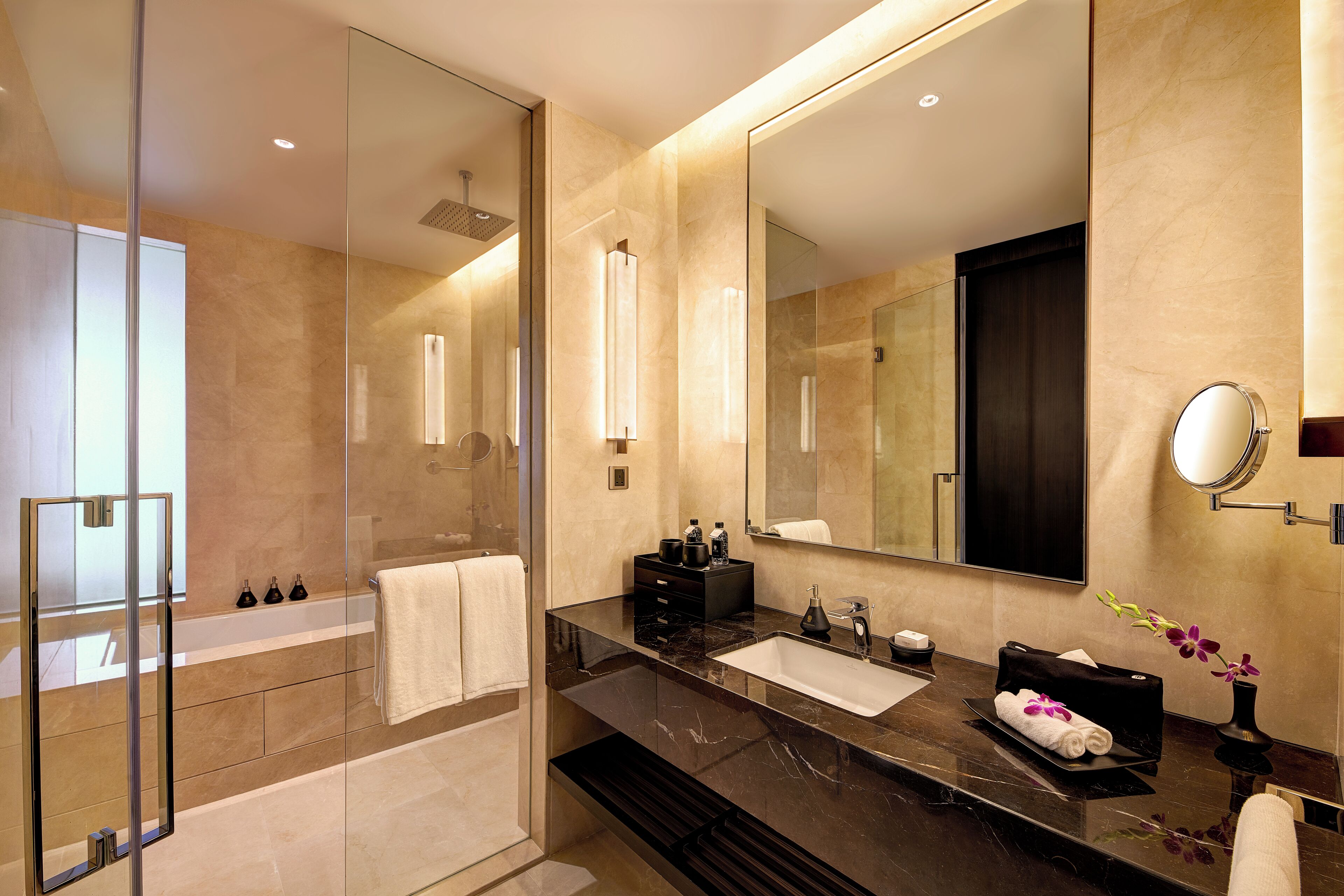 A modern bathroom with a glass-enclosed shower, a large mirror, a marble countertop, and a black sink.