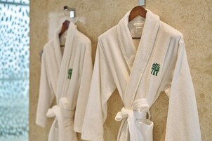 Two white bathrobes with green embroidery hanging on a wall.