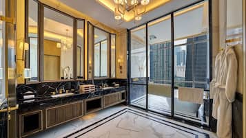 Un baño lujoso con un espejo grande, suelo de mármol y vistas a la ciudad a través de amplias ventanas.