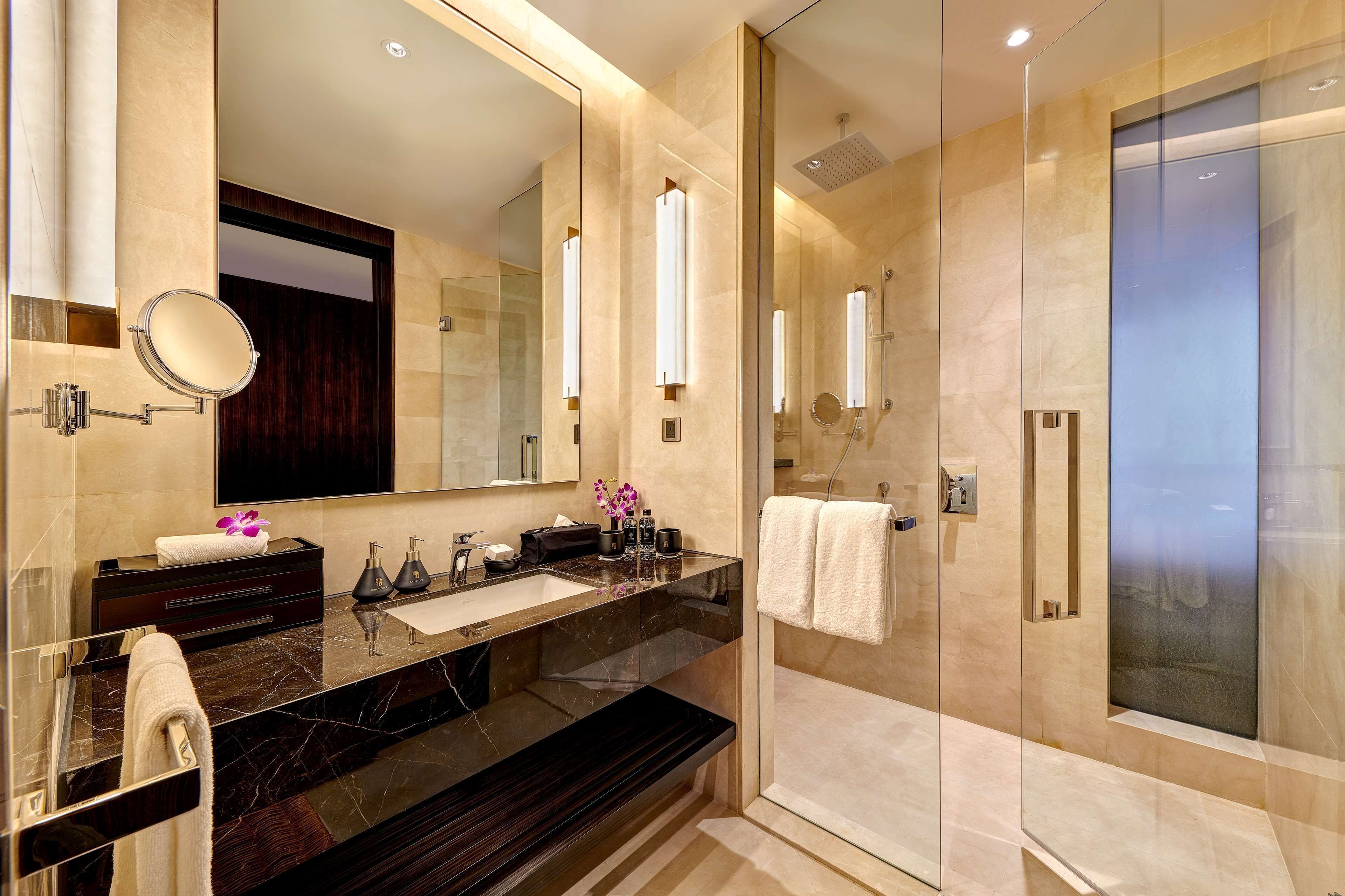 Un baño moderno con un espejo grande, encimera de mármol oscuro y ducha con mampara de cristal.