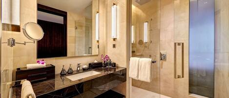 Un baño moderno con un espejo grande, encimera de mármol oscuro y ducha con mampara de cristal.