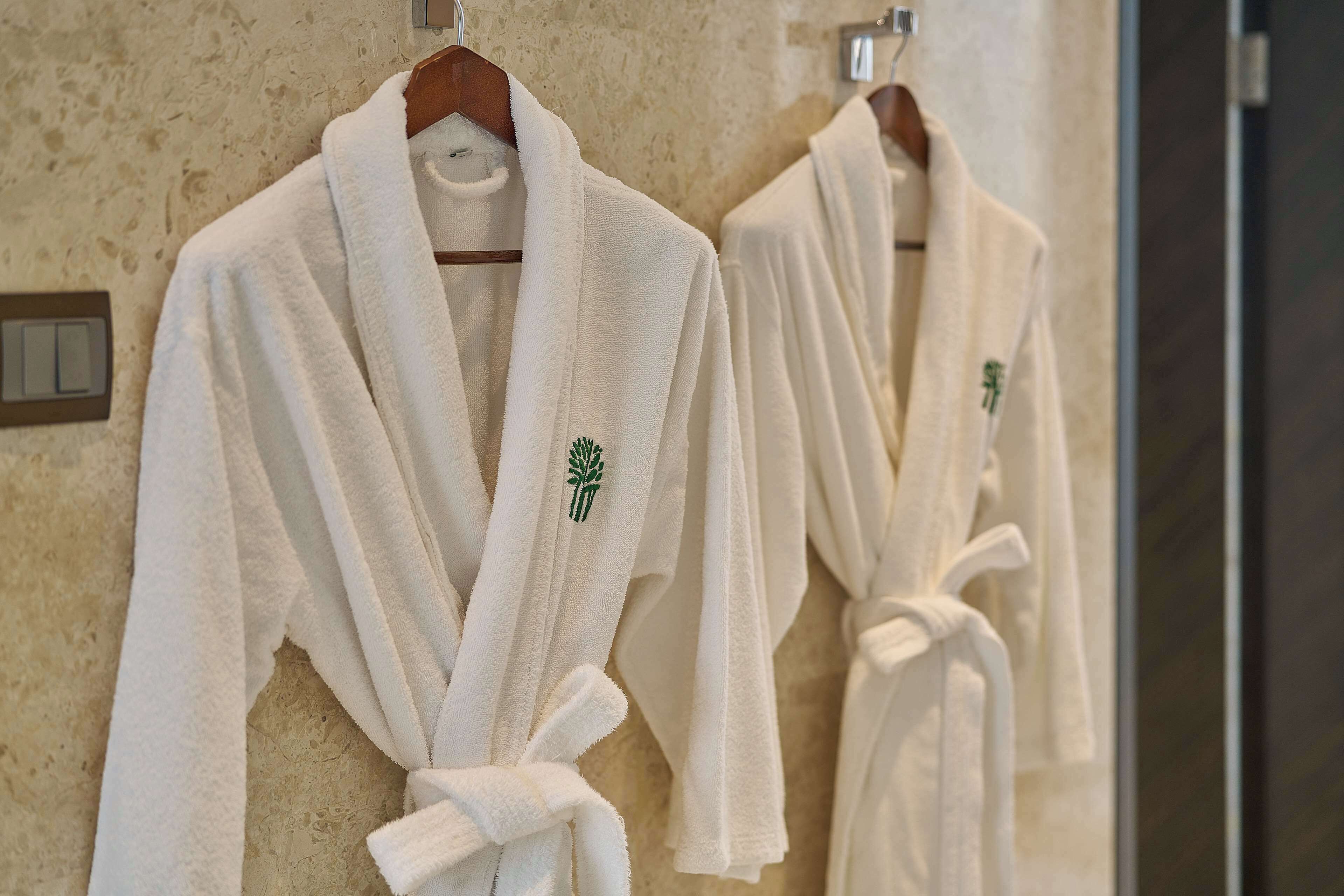 Two white robes hanging on a wall with a textured surface.