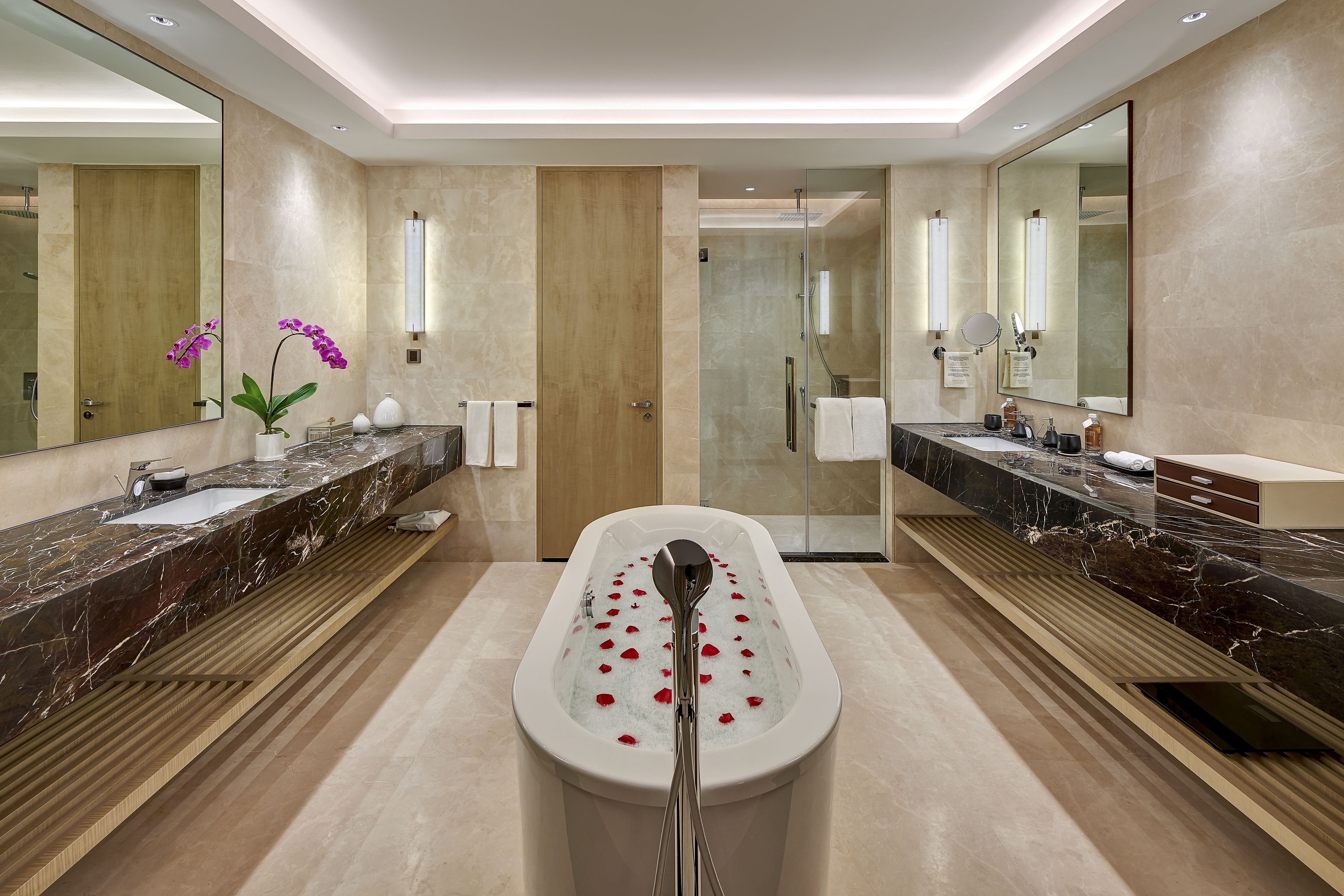 A modern bathroom with a marble vanity, a freestanding bathtub, and a glass shower enclosure.