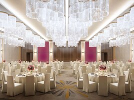 Un salón de banquetes con mesas redondas, sillas blancas y grandes candelabros de cristal.