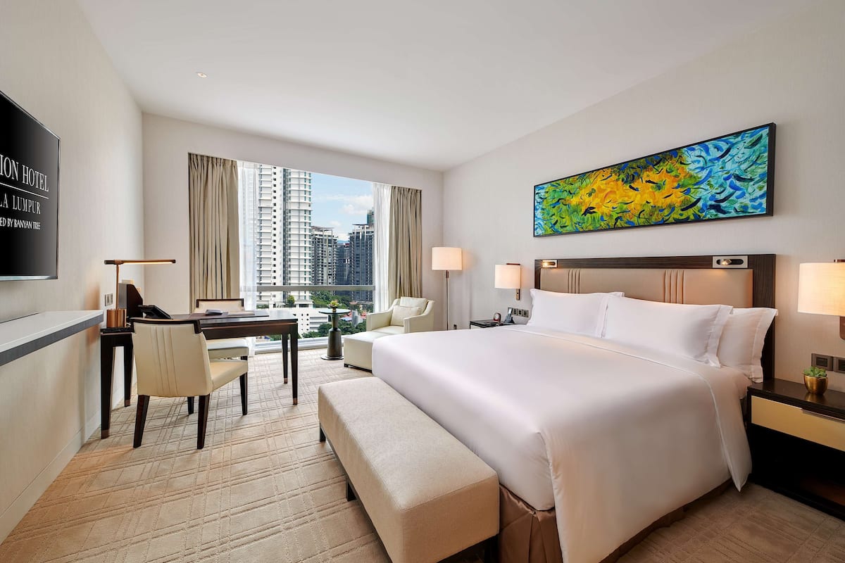 Ein Hotelzimmer mit einem großen Bett, einem Schreibtisch, einem Stuhl, einer Bank und Blick auf die Stadtlandschaft.