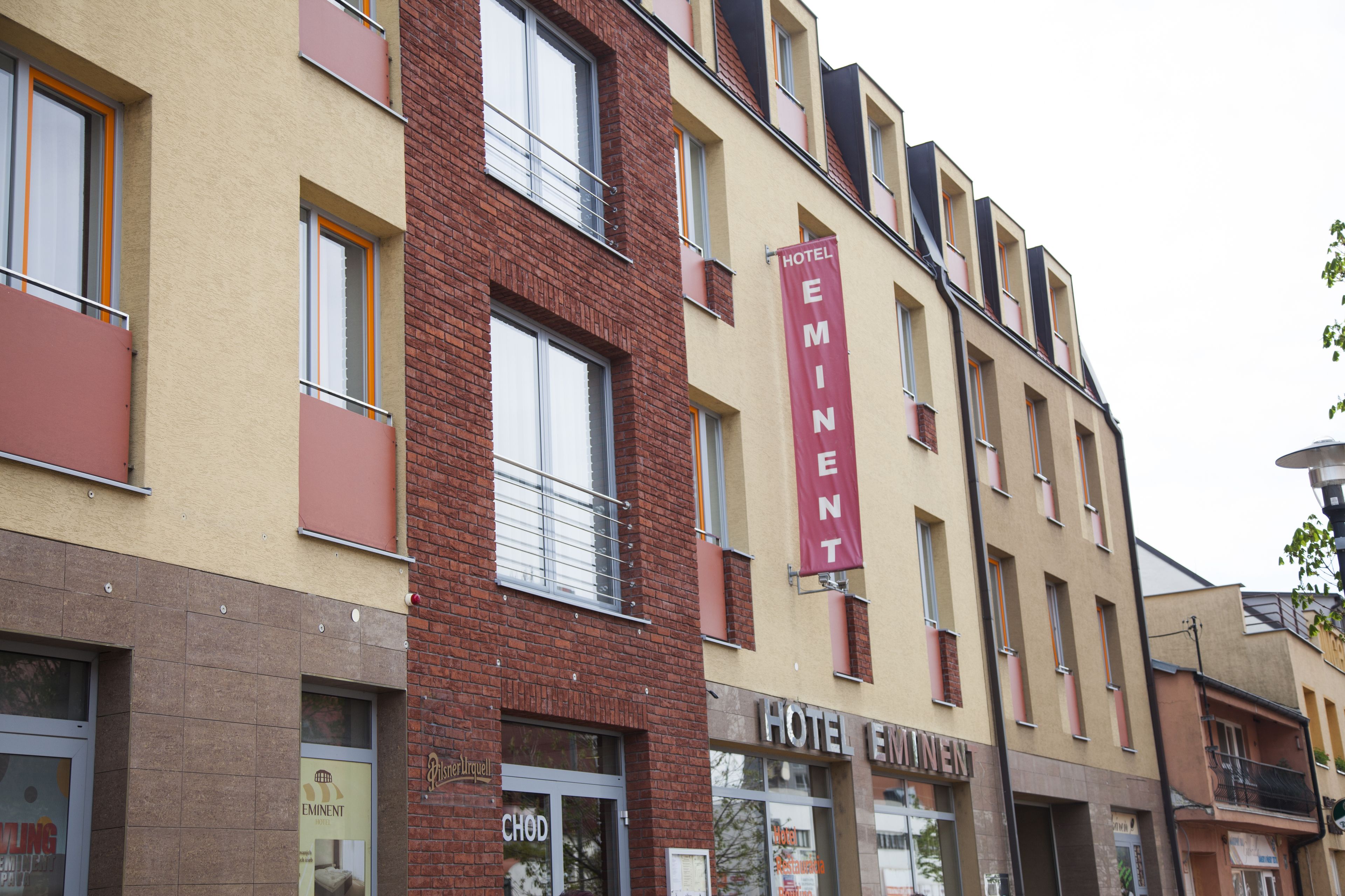 A hotel named 'Eminent' with a modern facade, featuring a prominent red banner, multiple balconies, and a variety of window styles.
