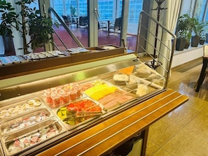 Un mostrador de buffet con diversos alimentos y vista al área de mesas al aire libre.